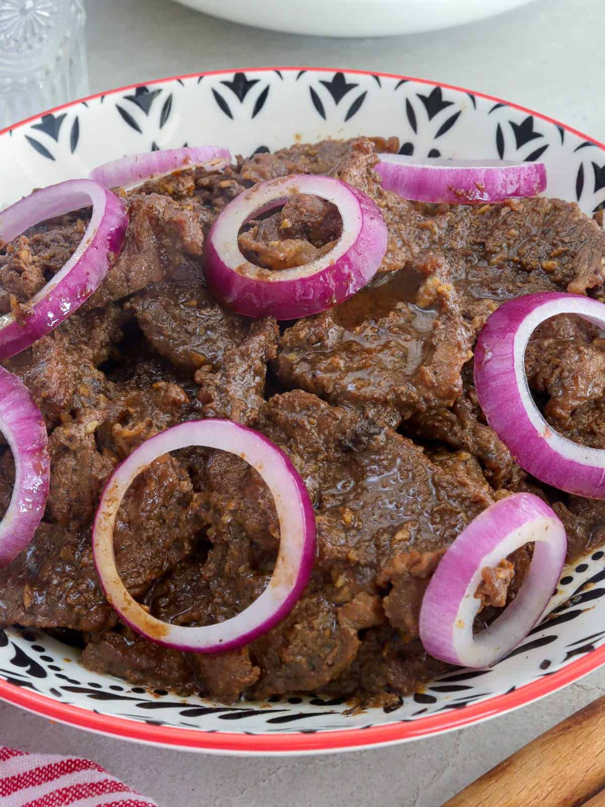 Filipino beefsteak with onions in a white serving bowl.