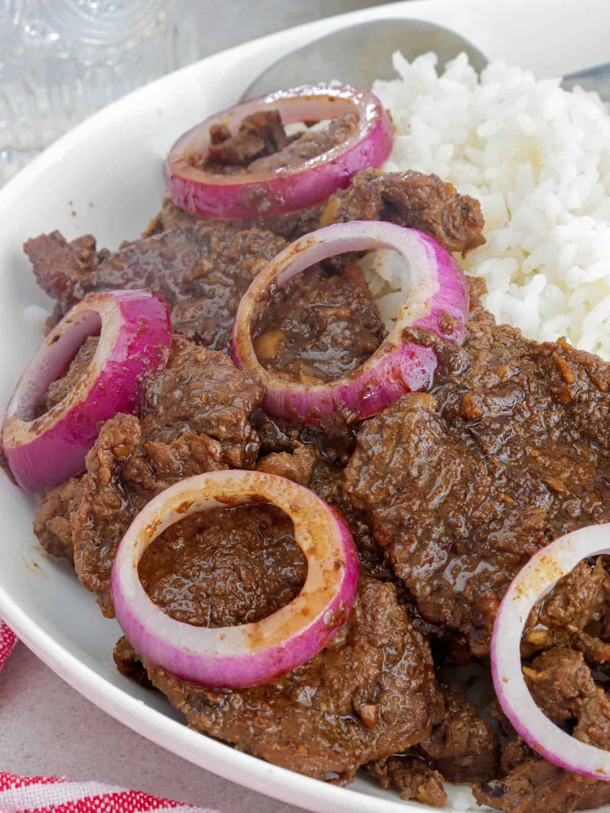 bistek Tagalog with onions over rice on a serving plate.