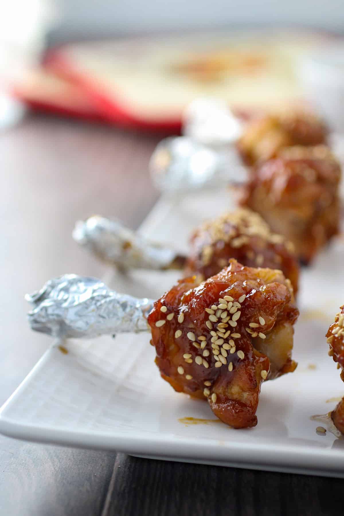 chicken lollipops seasoned with plum sauce on a white serving platter.