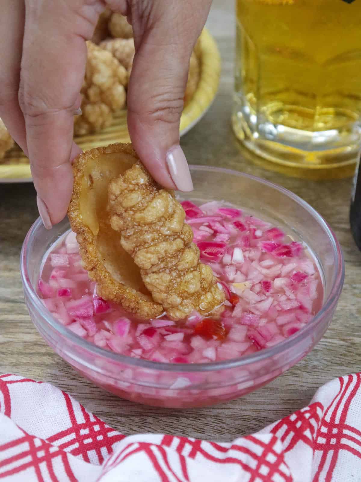 dipping pork cracklings in a bowl of spicy vinegar.