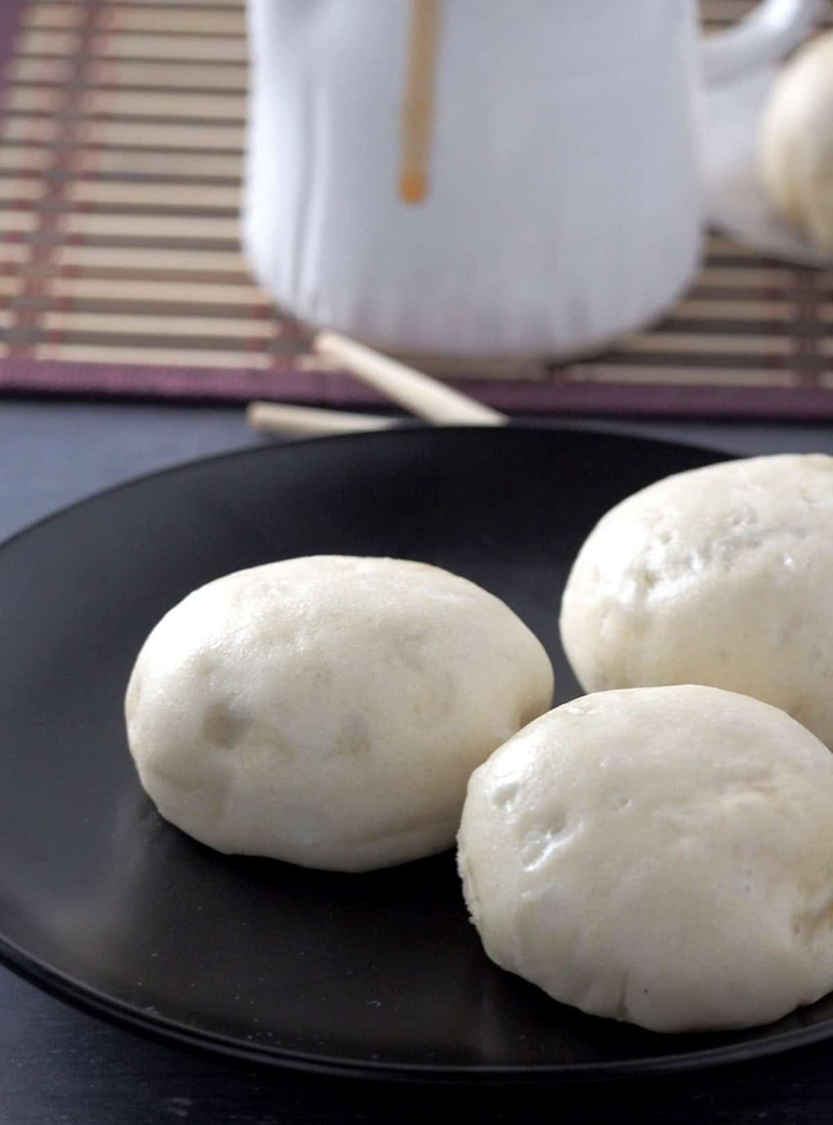 siopao buns on a black serving plate with siopao sauce on the side.