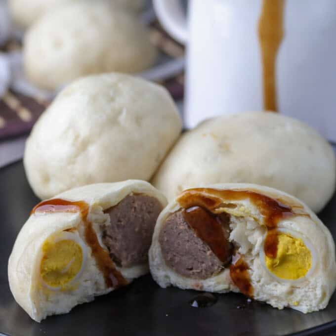 siopao buns cut in half on a black serving plate with siopao sauce on the side.