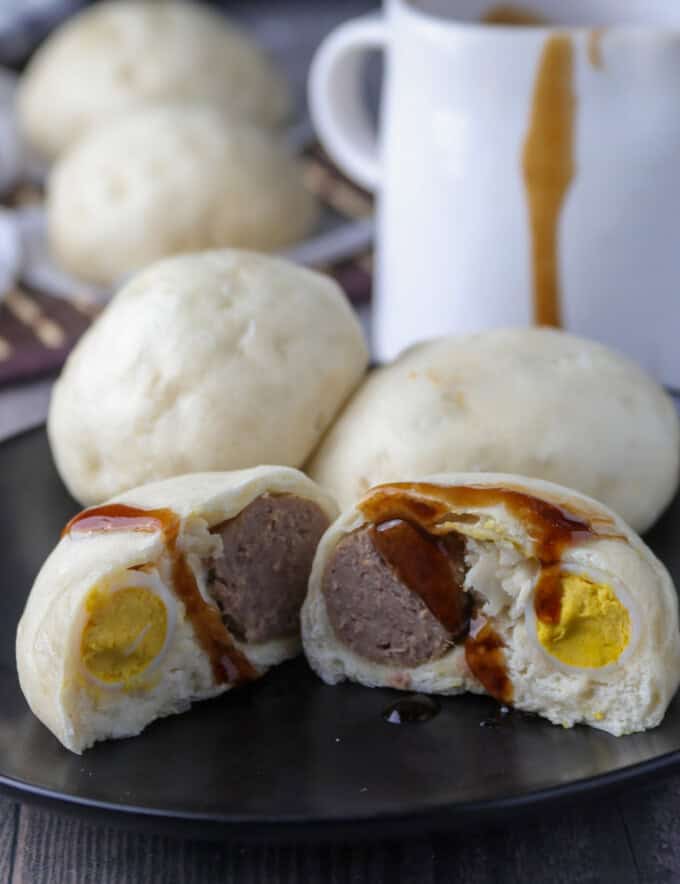 siopao buns cut in half on a black serving plate with siopao sauce on the side.