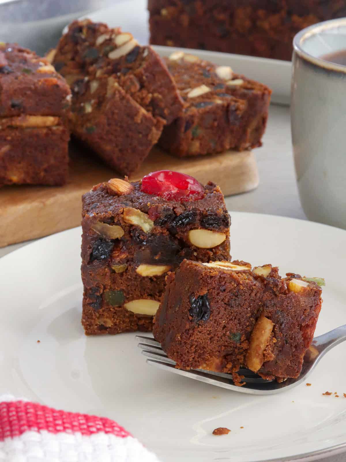 eating fruitcake with a fork on a serving plate with more slices on a cutting board in the background.