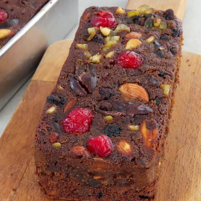 Holiday fruitcake with glazed fruits and nuts on a wooden cutting board.