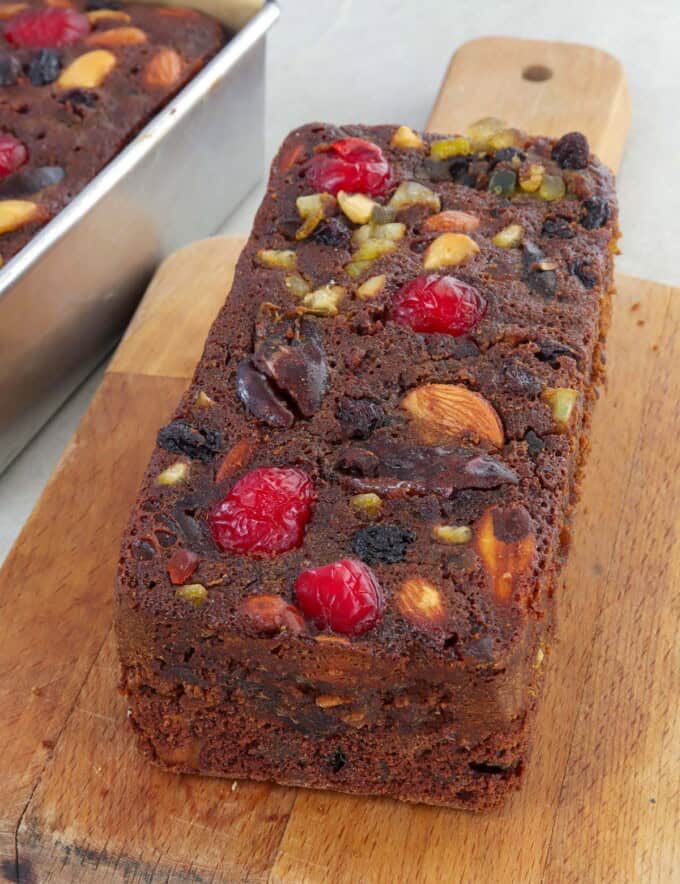 Holiday fruitcake with glazed fruits and nuts on a wooden cutting board.