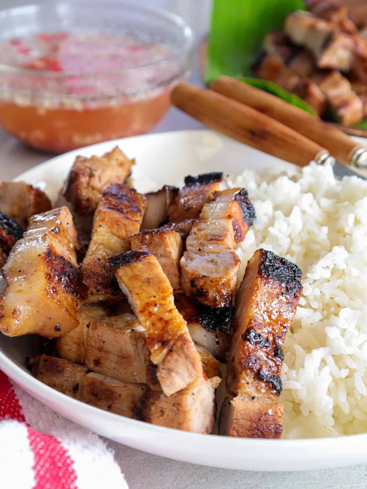 Filipino style grilled pork belly on a white plate with steamed rice.