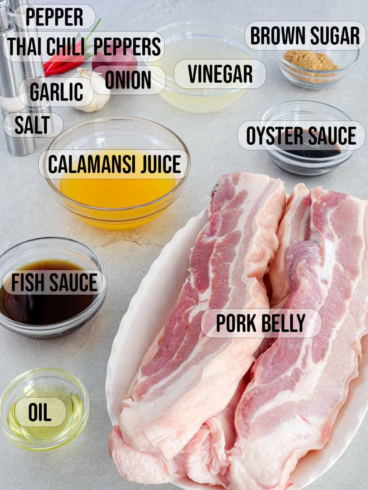 pork belly, calamansi juice, oyster sauce, soy sauce, garlic, oil, vinegar, brown sugar, onion, salt, pepper in bowls.