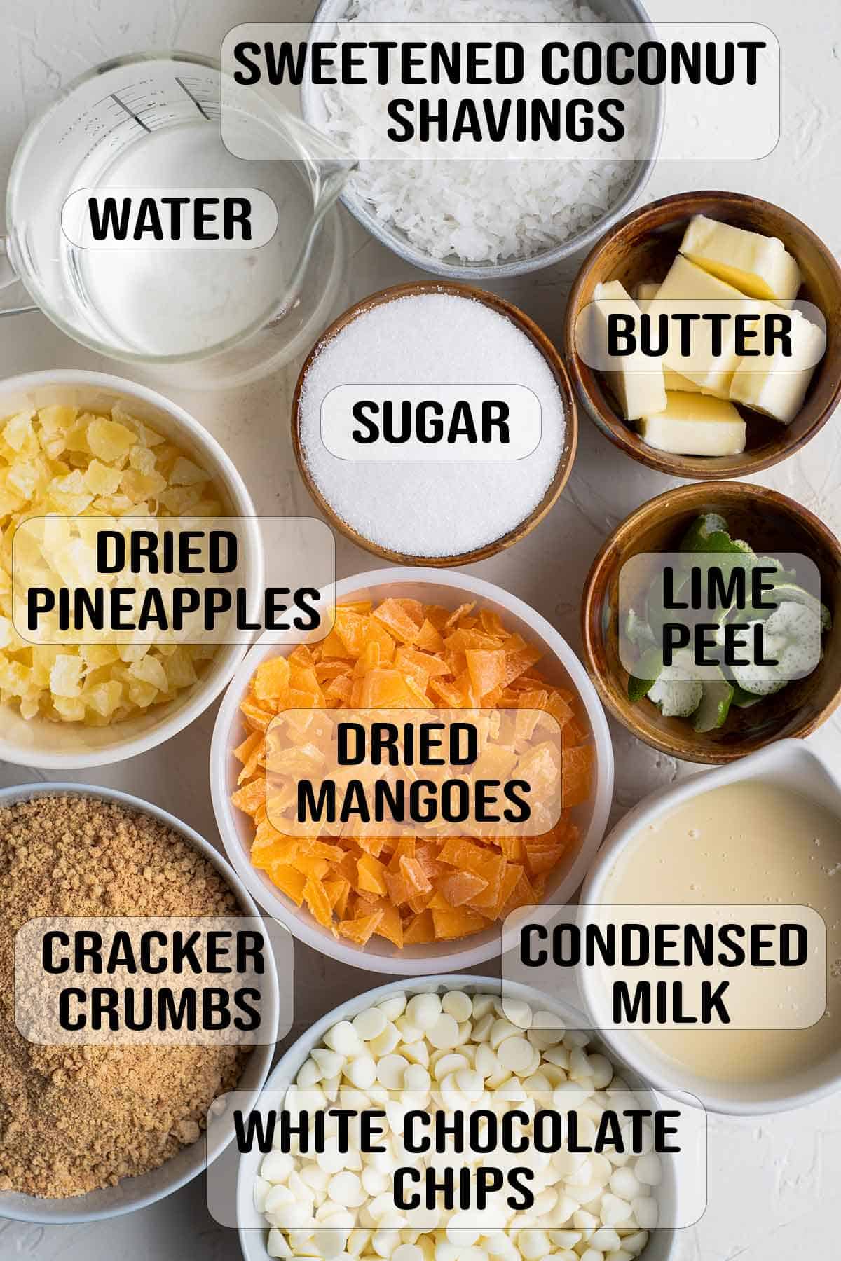 water, sugar, white chocolate chips,chopped dried mangoes, dried pineapples, candied lemon peels, graham cracker crumbs, condensed milk, butter, coconut shavings in bowls.