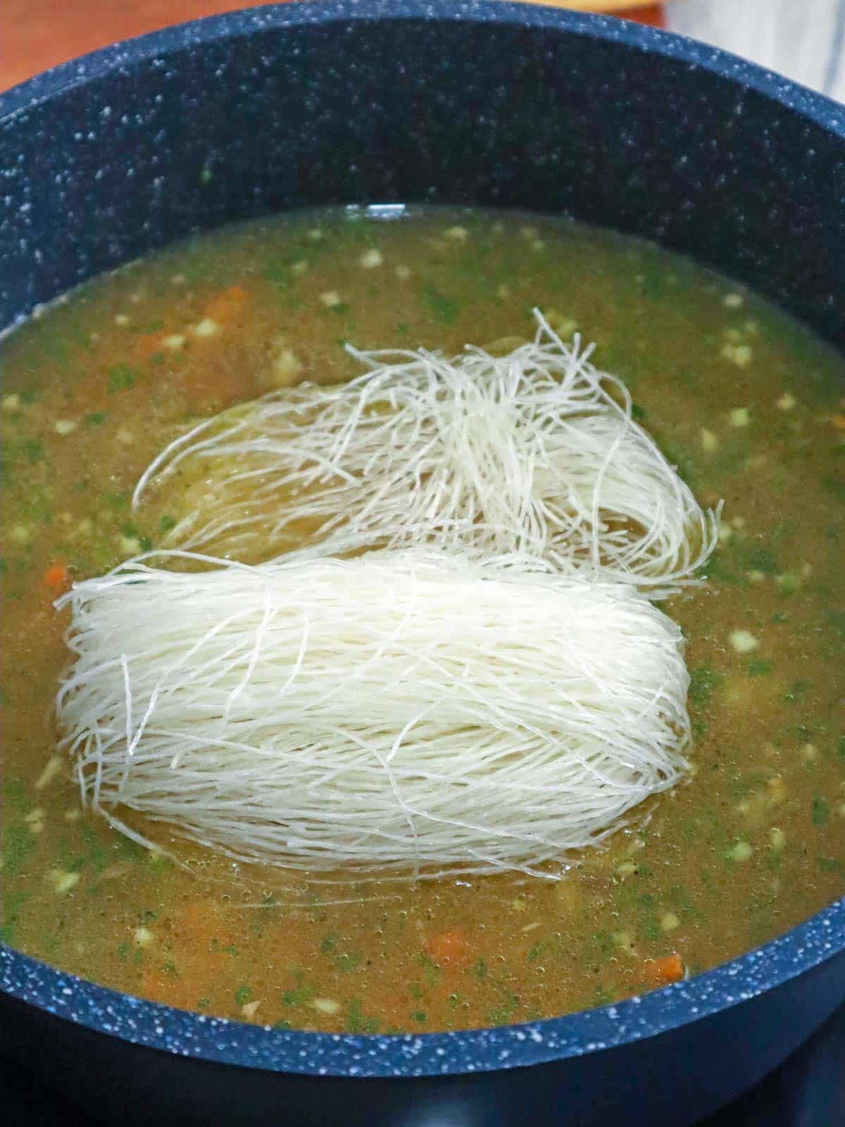 cooking cellophane noodles in broth in a pot.