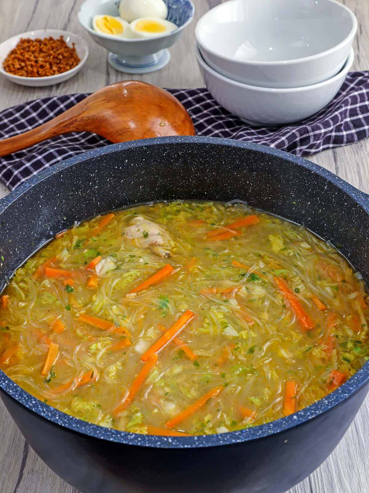 pot of chicken sotanghon soup with white bowls in the background.