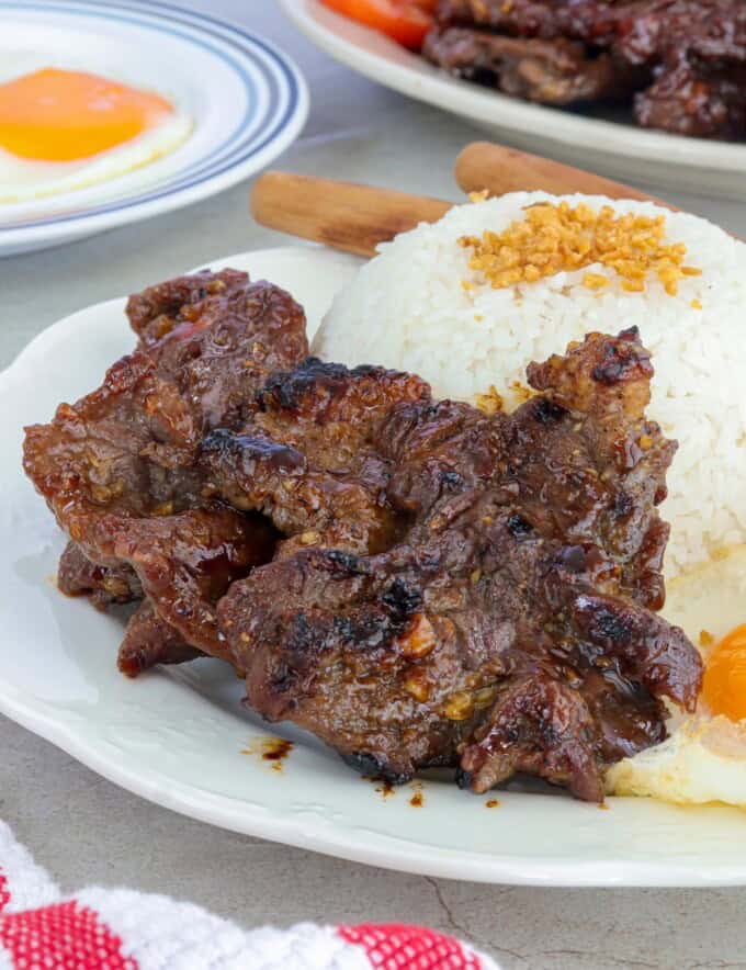 tapa damulag with garlic fried rice and sunny side-up eggs on a white plate.