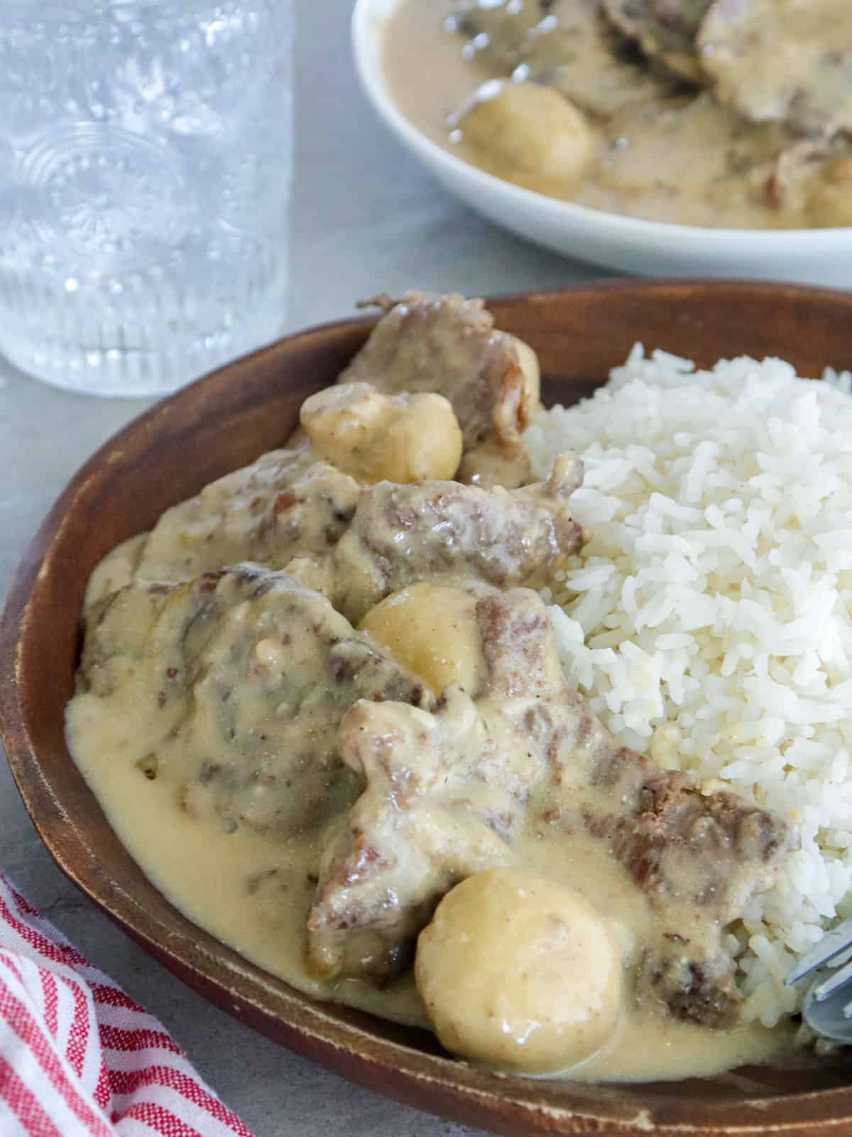 Beef in Creamy Mushroom Sauce over steamed rice on a wooden plate.