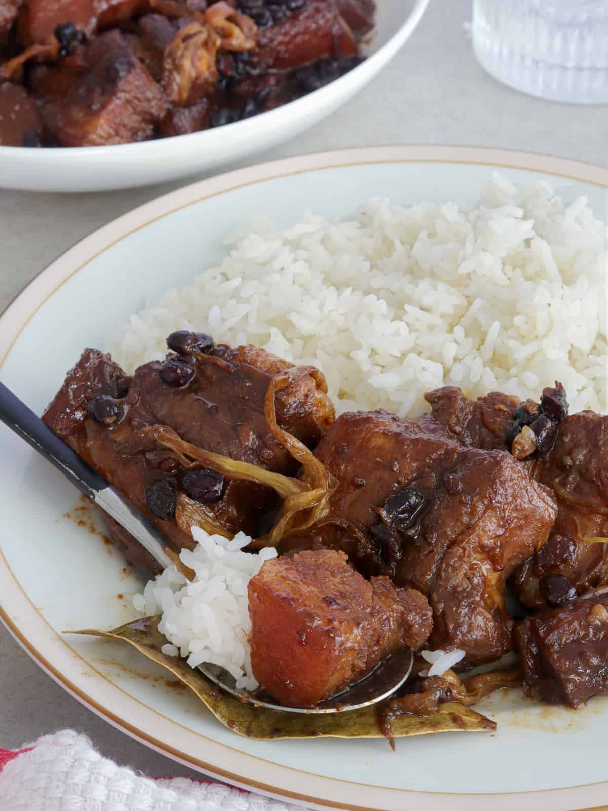 pork humba with steamed rice on the side on a white plate.