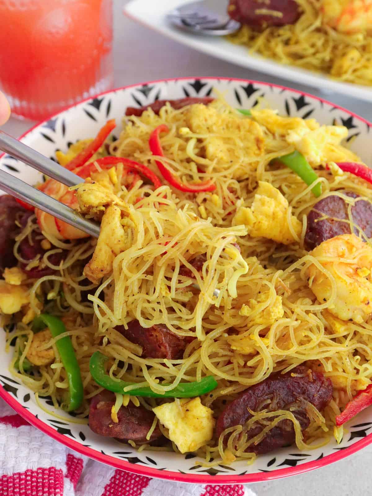 eating Singapore noodles with bell peppers, chicken, and sausage in a bowl.