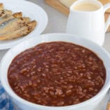 champorado in a white bowl with fried tuyo and evaporated milk in the background.