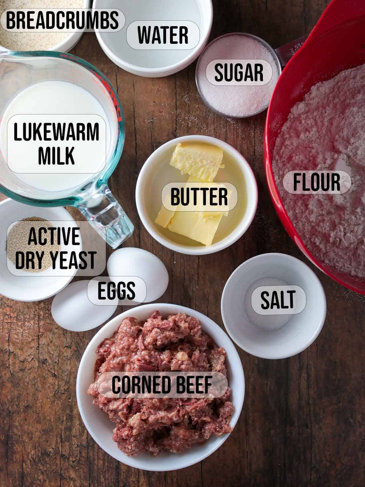 flour, corned beef, butter, eggs, yeast, milk, water, bread crumbs, sugar, salt in bowls.