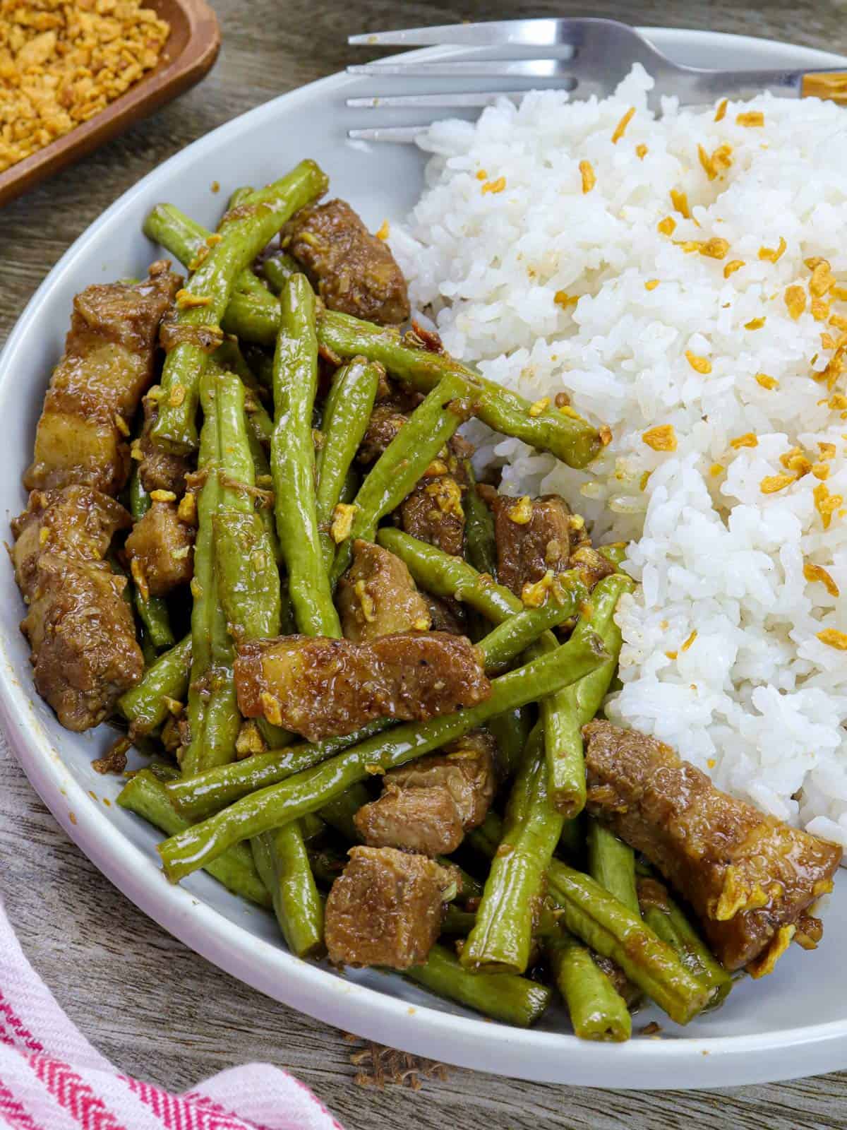 adobong sitaw with steamed rice on a white serving plate.