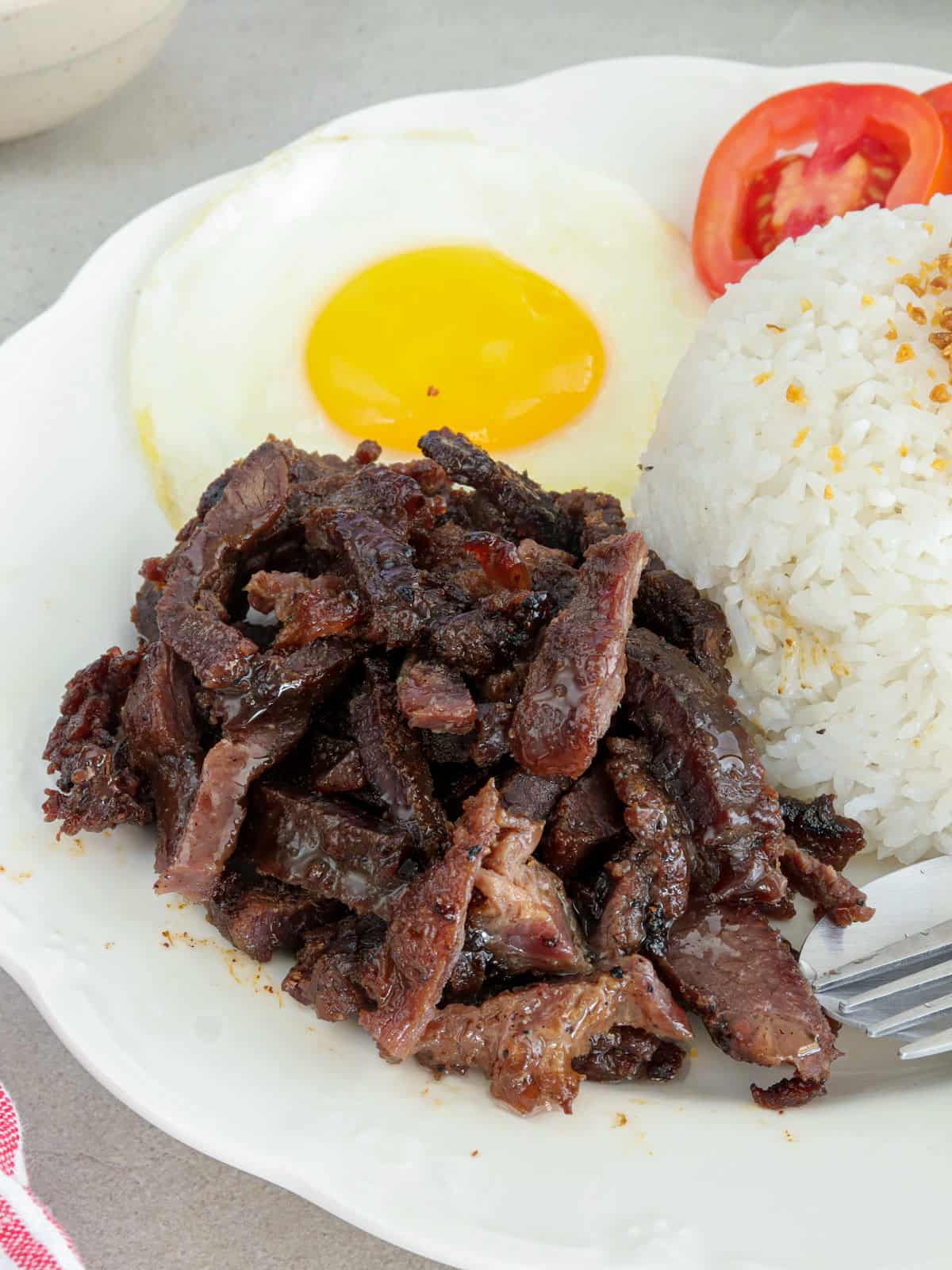 carabao beef tapa with sliced tomatoes on white platter.