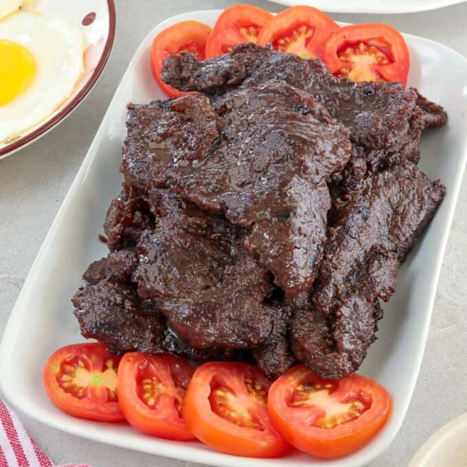 tapa damulag with garlic fried rice and sunny side-up eggs on a white plate.