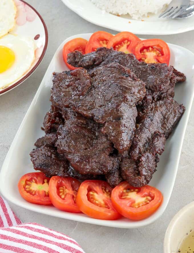 tapa damulag with garlic fried rice and sunny side-up eggs on a white plate.