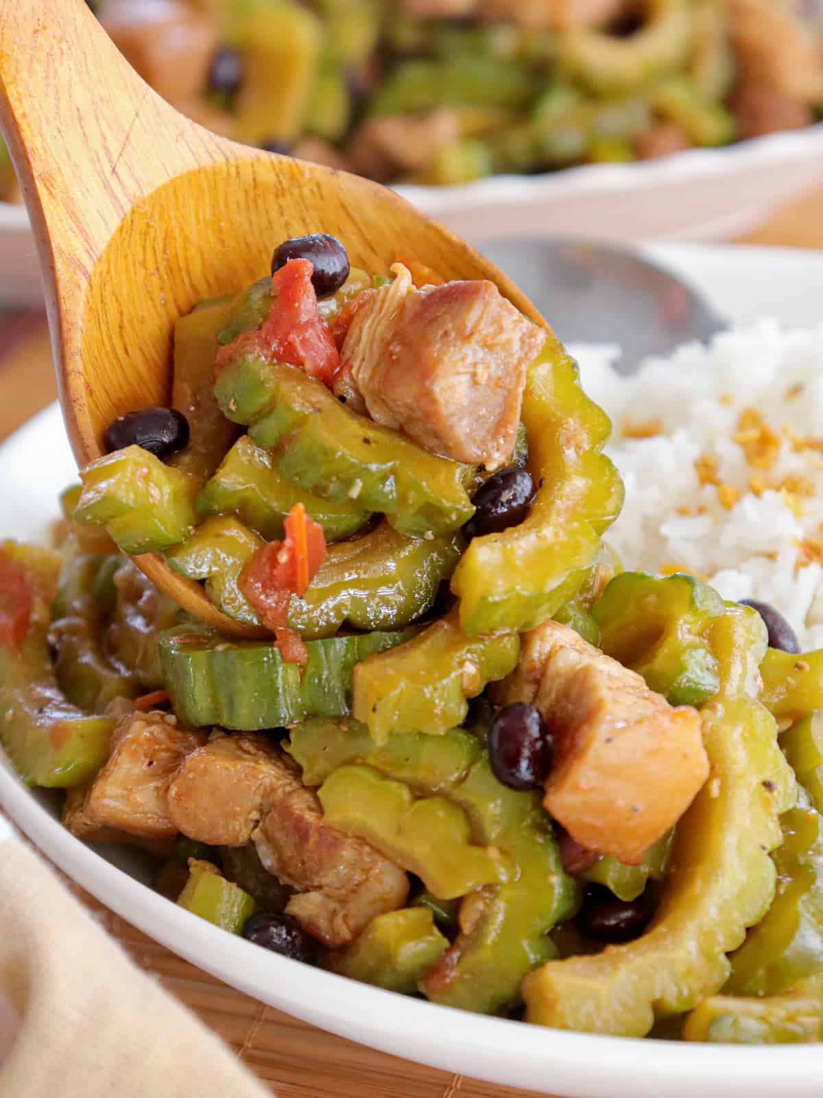 serving bittermelon with pork and fermented black beans with a wooden spoon on a plate of steamed rice.