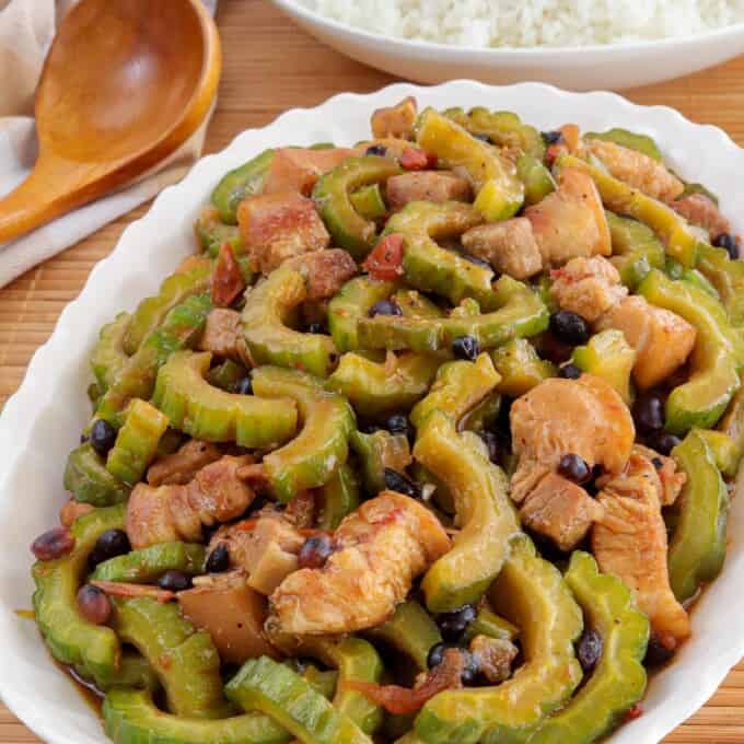 Ampalaya con Tausi on a white platter with a plate of steamed rice in the background.