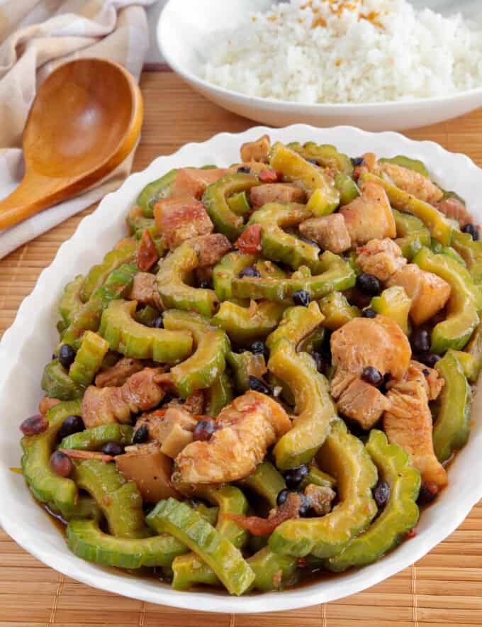 Ampalaya con Tausi on a white platter with a plate of steamed rice in the background.