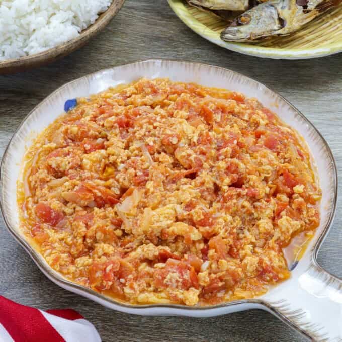 kultyas in a white bowl with fried fish and steamed rice in the background.