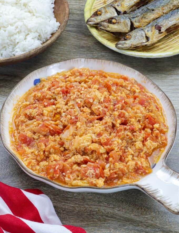 kultyas in a white bowl with fried fish and steamed rice in the background.