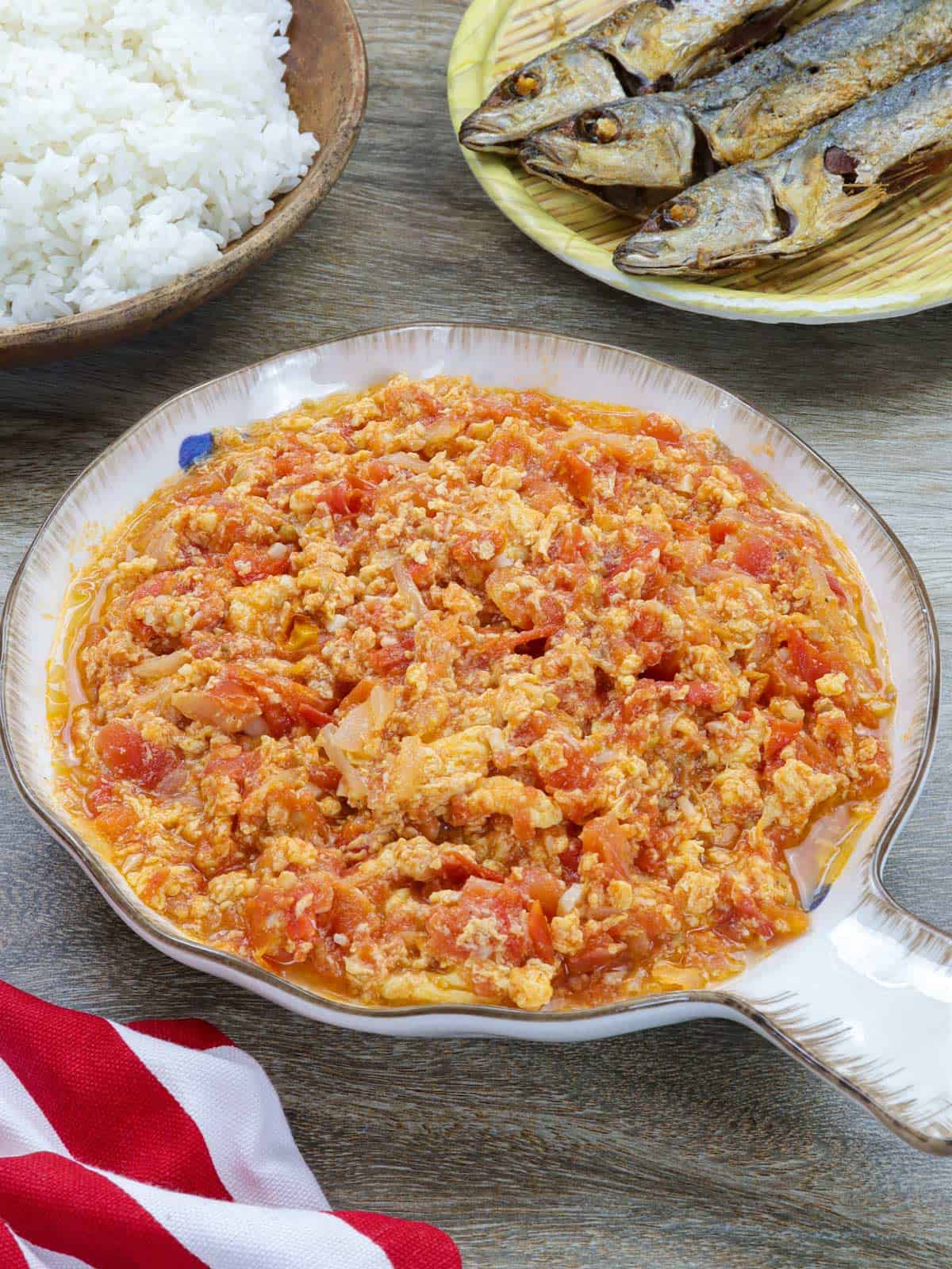 kultyas in a white bowl with fried fish and steamed rice in the background.