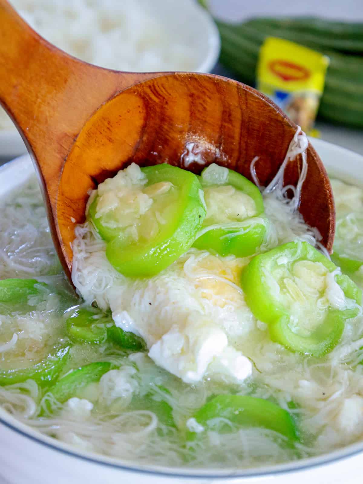 serving miswa patola with poached eggs in a white bowl with a wooden ladle.