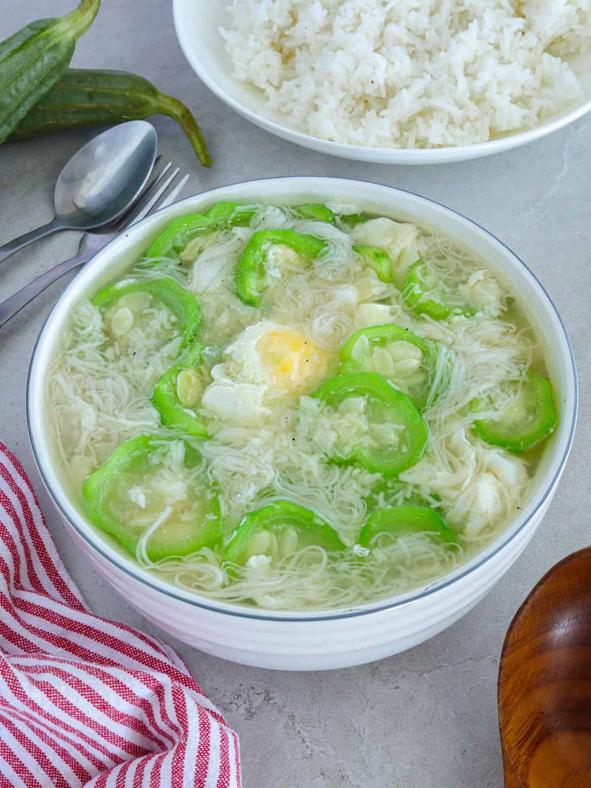 Miswang Ebun with Patola in a white bowl with a plate of steamed rice in the background.