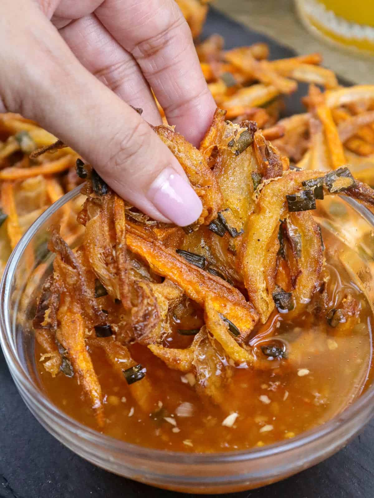 dipping sibuyas na okoy in a small bowl of spicy vinegar.