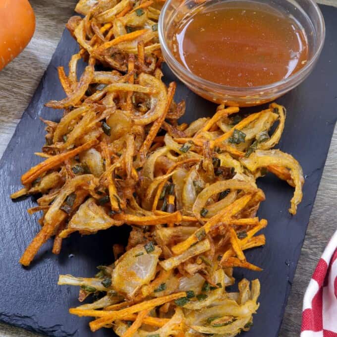 sweet onion fritters on a black serving platter with a small bowl of spicy vinegar.