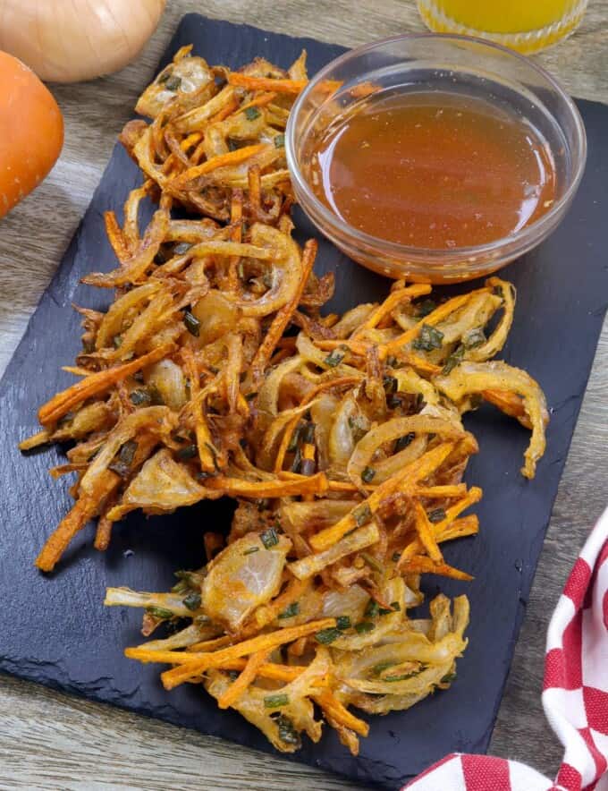 sweet onion fritters on a black serving platter with a small bowl of spicy vinegar.