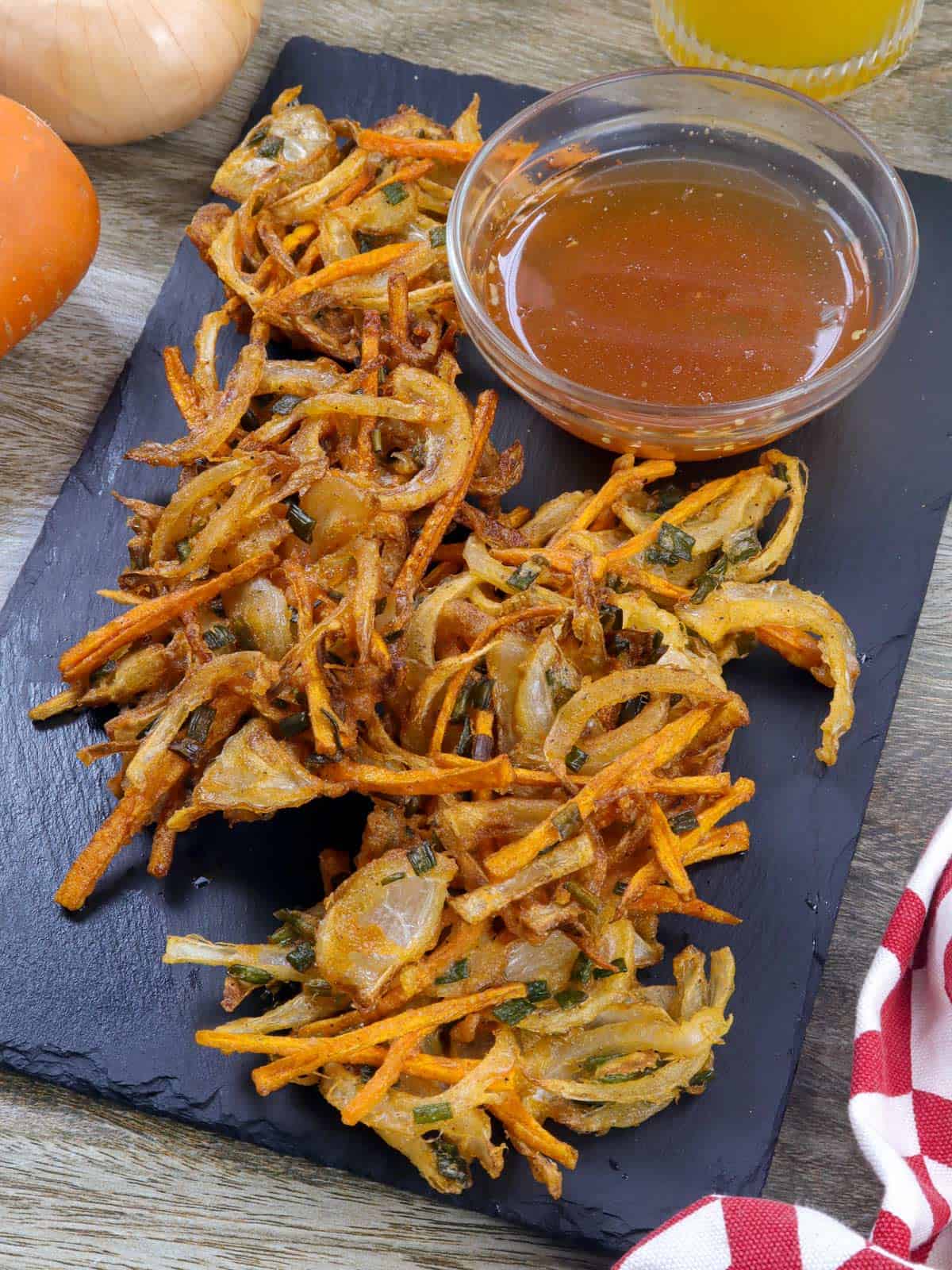 sweet onion fritters on a black serving platter with a small bowl of spicy vinegar.