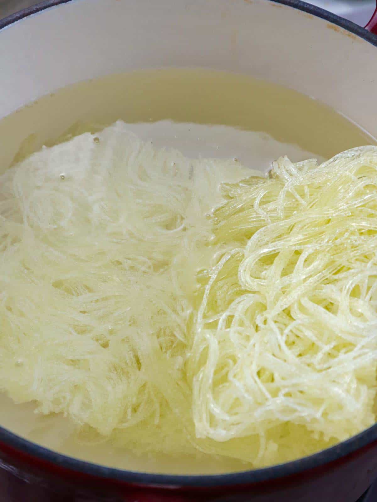 cooking palabok noodles in a pot of water.