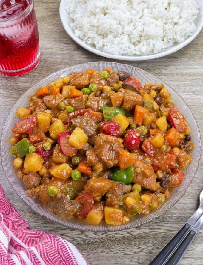 Filipino Menudo on a serving platter with plate of steamed rice in the background.