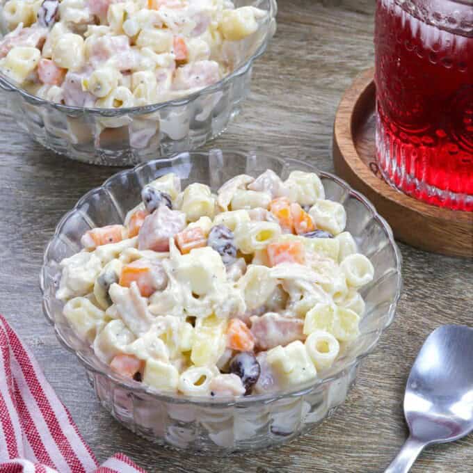 Macaroni Ham Salad in a bowl with a glass of juice in the background.