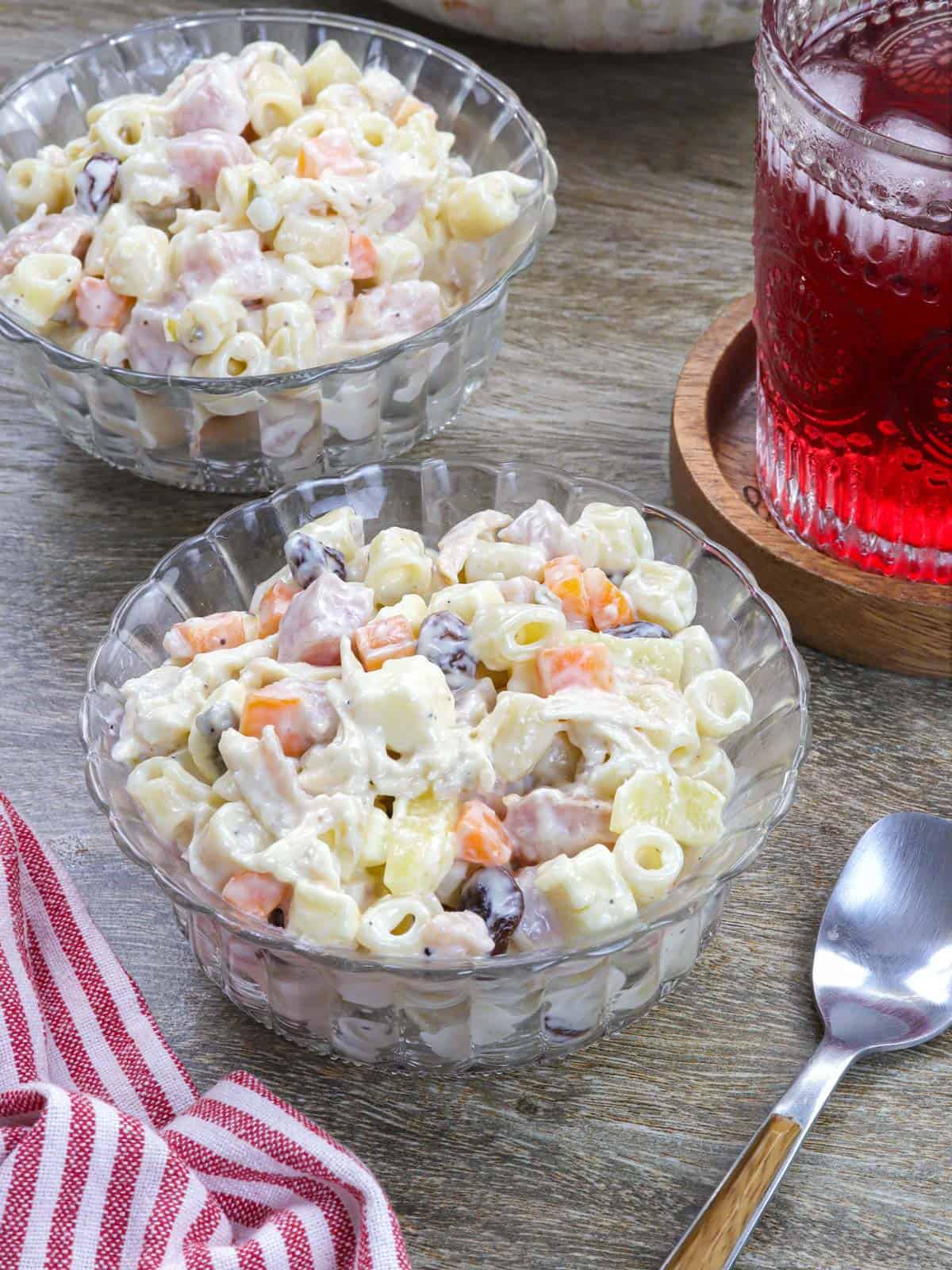 Macaroni Ham Salad in a bowl with a glass of juice in the background.