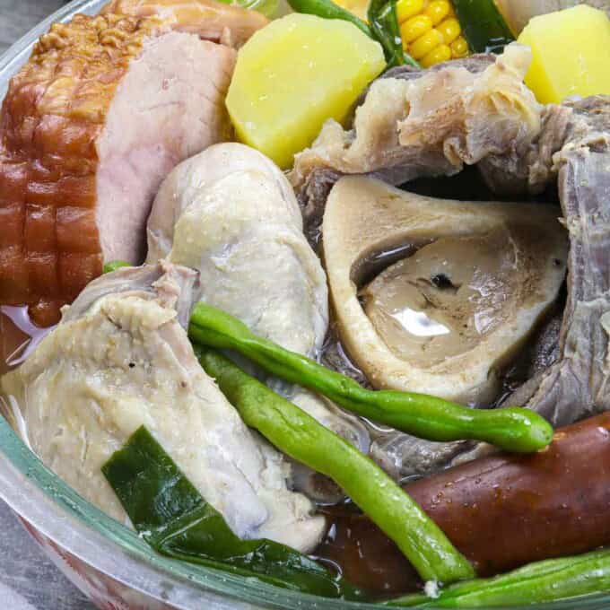 a bowl of nilagang pasko with ham, beef, chicken, pork, sausage, and vegetables.