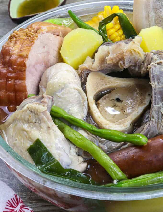 a bowl of nilagang pasko with ham, beef, chicken, pork, sausage, and vegetables.