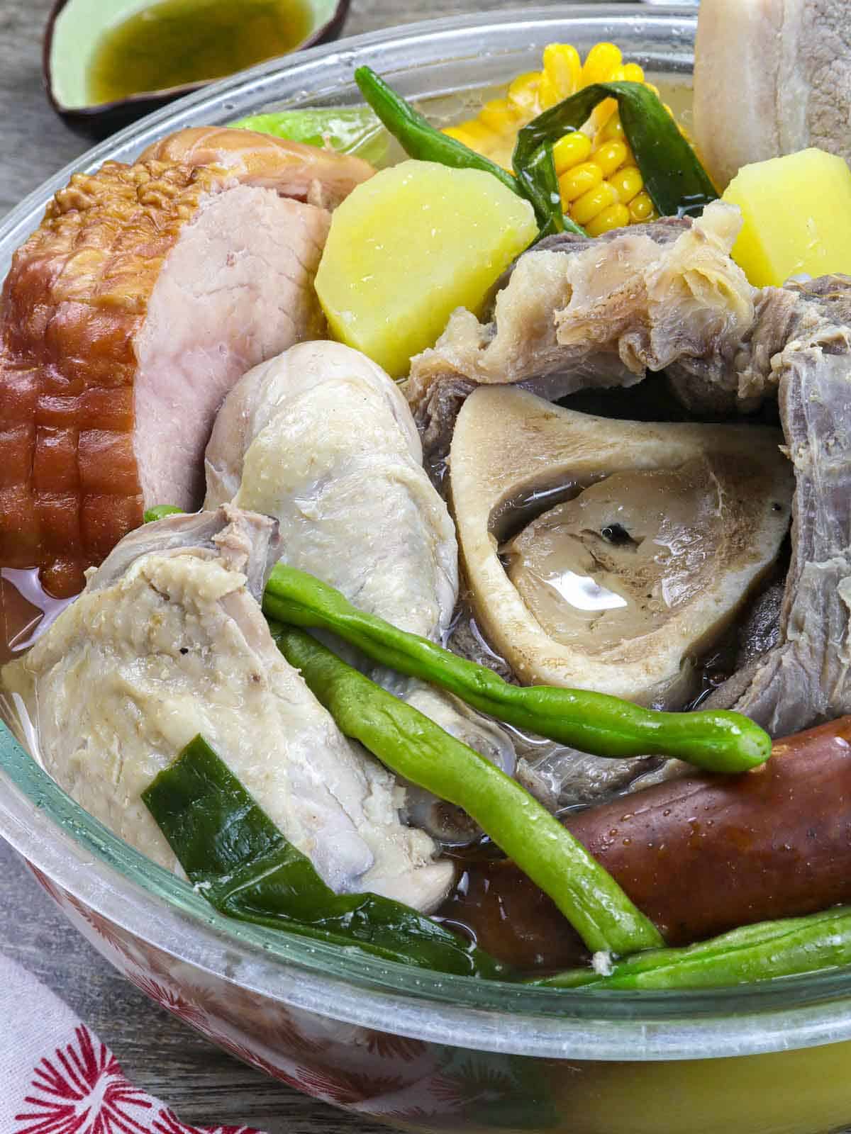 a bowl of nilagang pasko with ham, beef, chicken, pork, sausage, and vegetables.